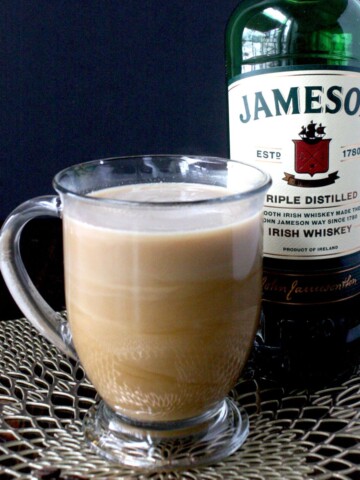 A photo of an irish coffee with whiskey, coffee and cream in front of a bottle of Jameson whiskey