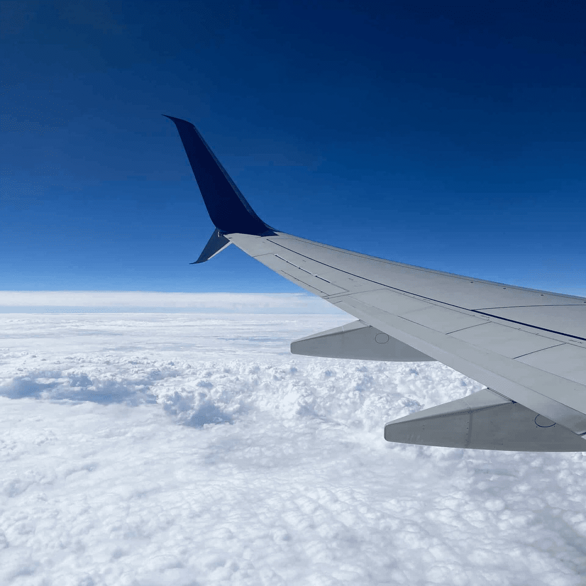 Photo of airplane wing in sky with clouds