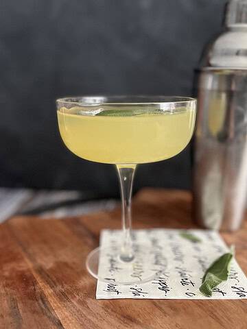 Photo of sage gimlet on a wooden tray with cocktail shaker in the background