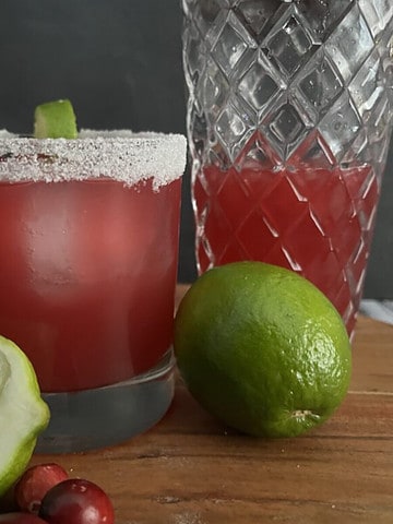 Photo of a winter margarita with shaker, cranberries and limes