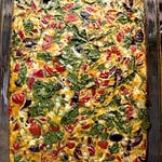 Photo of an egg bake with Mediterranean flavors--peppers, olives, feta cheese and spinach, all in a glass 9x13 casserole dish