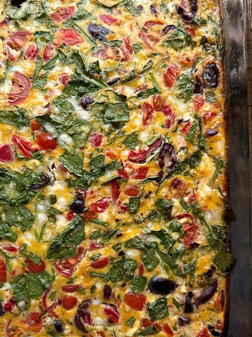 Photo of an egg bake with Mediterranean flavors--peppers, olives, feta cheese and spinach, all in a glass 9x13 casserole dish