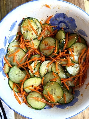 A photo of sliced carrot and cucumber salad in a white bowl on a cutting board.