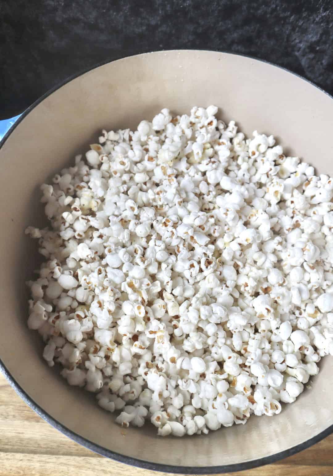 Popped popcorn in a blue enameled cast iron dutch oven sitting on a wooden cutting board.