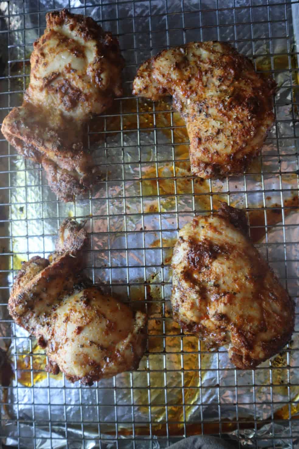 A baking sheet and baking rack stacked with four boneless skinless baked chicken thighs on top.