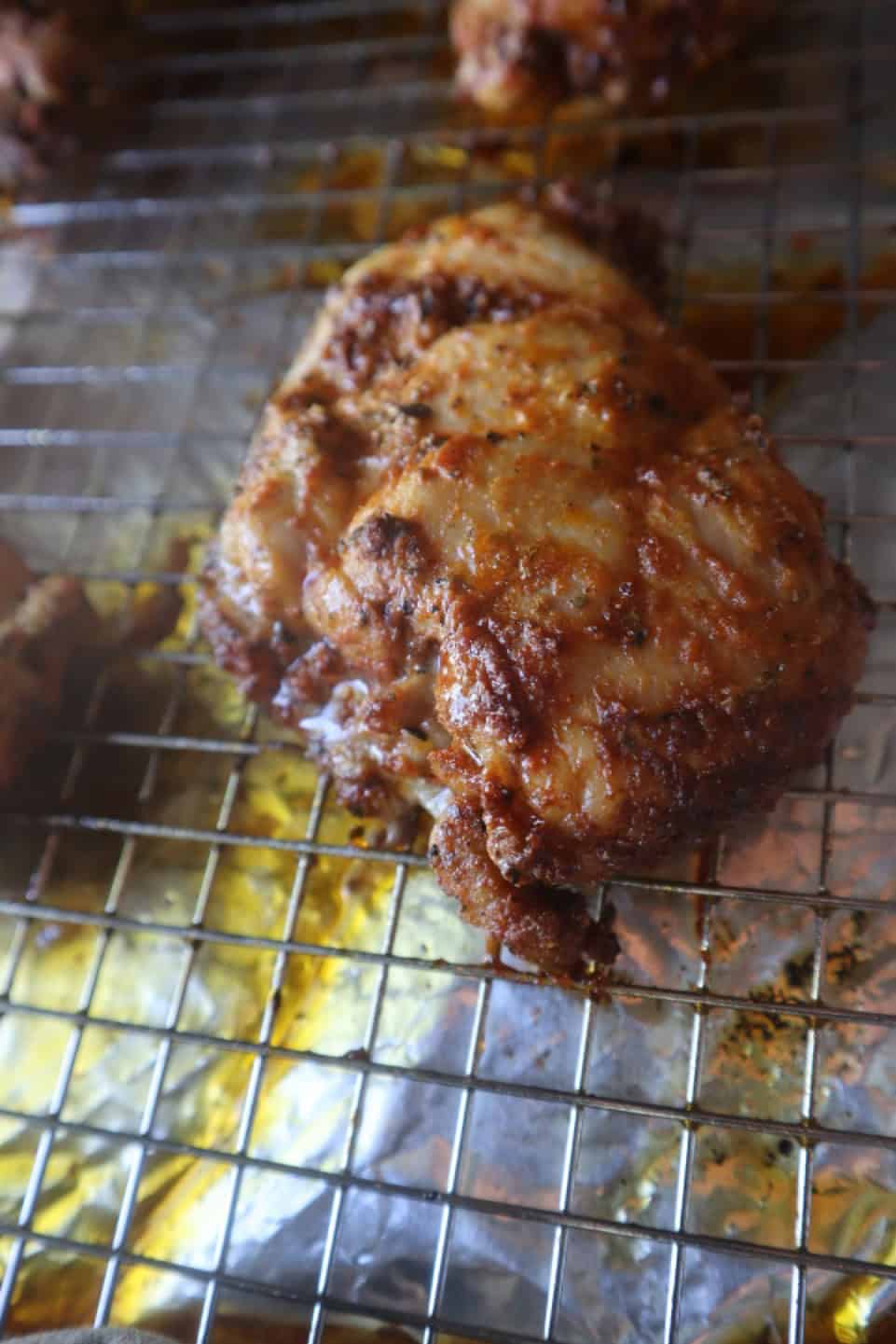 A baked boneless skinless chicken thigh straight out of the oven on a baking rack on a baking sheet.