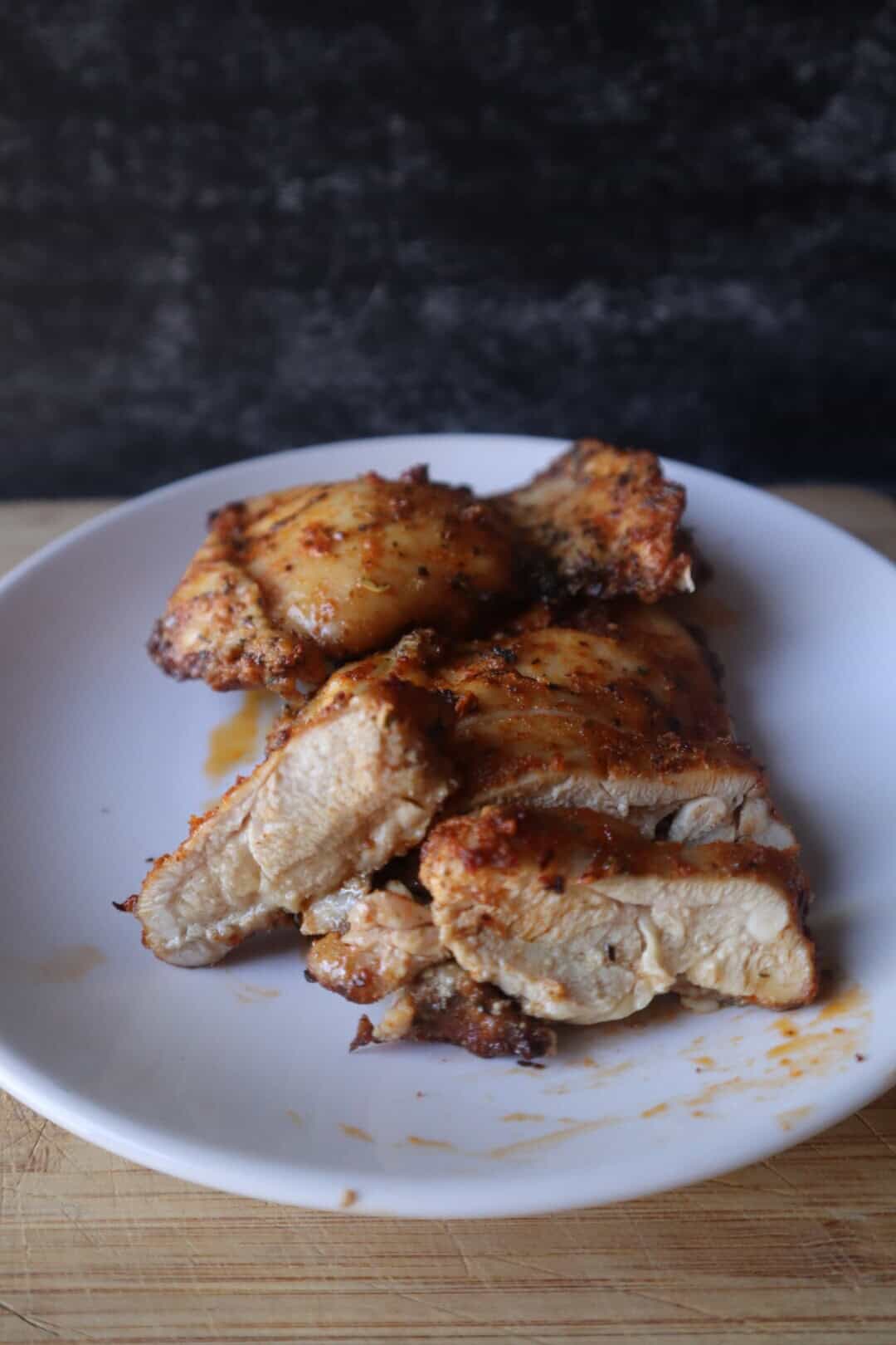 A photo of juicy baked boneless skinless chicken thighs on a white plate.