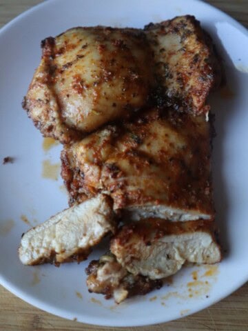 A photo of two baked boneless skinless chicken thighs on a white plate